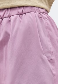 Κοντινή λήψη ανοιχτό μωβ ελαστικών παντελονιών με πλαϊνή τσέπη και καφετί τοπ που φαίνεται μερικώς πάνω από τη μέση.