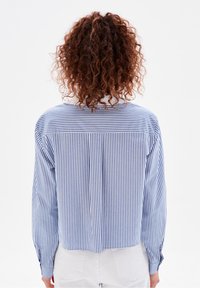 Camicia a maniche lunghe a righe con colori blu e bianchi, dotata di un pleat posteriore e design cropped. Tessuto testurizzato con una finitura morbida.