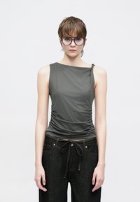 Γκρι αμάνικη μπλούζα με πιετά υφή και ασύμμετρο ντεκολτέ, συνδυασμένη με χαλαρά μαύρα τζιν παντελόνια με κορδόνι στη μέση.