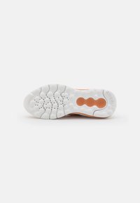 Suola di scarpa in gomma bianca con un motivo di presa texturizzato e dettagli arancioni. Include fori di ventilazione circolari e scanalature di flessione per una maggiore flessibilità.