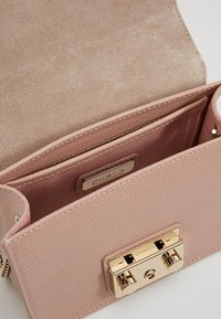 Borsa a tracolla in pelle rosa chiaro con texture, chiusura a scatto dorata, patta aperta, tasca interna visibile e etichetta "Furla Genuine Leather" all'interno.