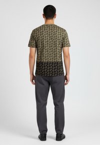 Krátký rukáv tričko olivově zelené barvy s černým abstraktním vzorem, s rovný střih. Nosené s tmavě šedými kalhotami a černými botami.