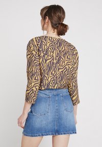 Brown and yellow-patterned top with three-quarter sleeves, paired with a blue denim mini skirt featuring two back pockets.