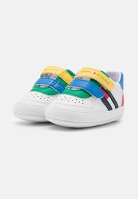 Białe sneakersy z wielokolorowymi akcentami w zielonym, niebieskim, żółtym i czerwonym. Posiadają regulowane paski i perforowane detale. Gładka struktura.