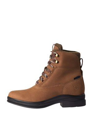 Botín marrón de cuero impermeable con suela negra, cuello de tela y cordones rojo-marrón sujetos con ojales de metal.