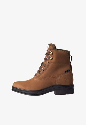 Bottine en cuir marron imperméable avec semelle noire, col en tissu et lacets rouge-brun fixés par des œillets métalliques.