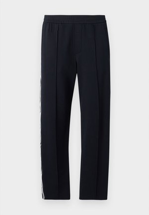 Schwarze, taillierte Hose mit elastischem Bund, zwei seitlichen Taschen und einem weißen Streifen, der das äußere Bein hinunterläuft. Glatte Textur.