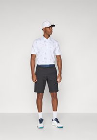 White short-sleeve polo shirt with blue sketches, paired with dark shorts and white shoes. Worn with a white cap and blue belt.