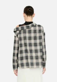 Schwarz-weißer karierten Hemd mit übergroßem Design, das überschnittene Schultern und eine lockere Passform aufweist. Glattes Material mit einer weichen Textur.