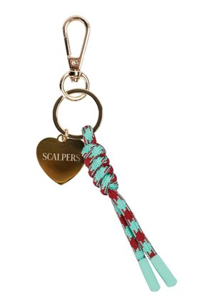 Llavero de metal dorado con clip, etiqueta en forma de corazón grabada con "SCALPERS," y cordón trenzado anudado en azul verdoso y rojo.