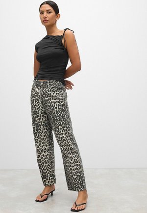 Svart åtsittande topp med en axelrem, i kombination med lösa byxor i leopardmönster. Modellen bär svarta sandaler med remmar. Ljust bakgrund.