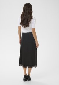 Jupe midi en satin noir avec un ourlet en dentelle, présentant une texture lisse et une coupe ajustée, associée à un haut blanc moulant et des talons noirs.