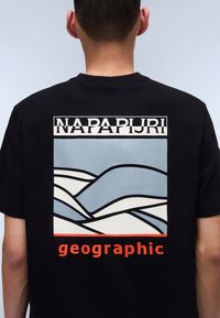 Tricou negru cu un imprimeu grafic colorat pe spate: modele ondulate de culoare albastră deschisă și albă, logo-ul "NAPAPURI" și textul "geographic" în culoarea portocalie.