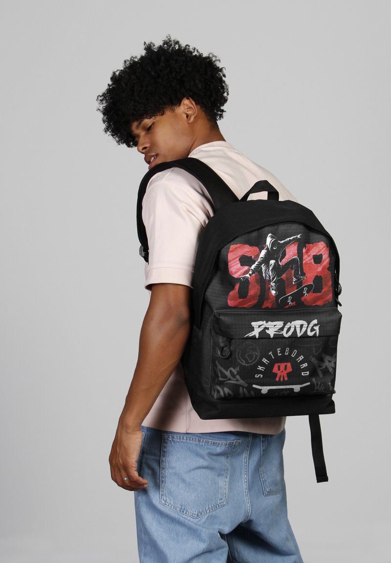 Mochila negra con diseños gráficos en rojo y blanco, que presenta motivos de patineta, correas de hombro acolchadas y un bolsillo frontal con cremallera.
