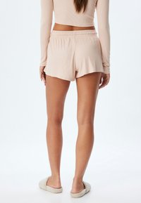 Lichtroze geribde shorts met een elastische tailleband, voorzien van een uitlopende zoom en een relaxte pasvorm, gecombineerd met zachte, harige slippers.