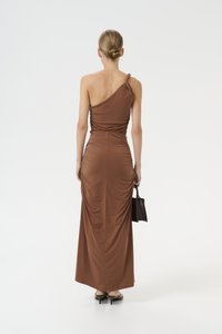 Brown, one-shoulder dress made of sleek fabric. Fitted design with gathered side details. Worn with a small black handbag, sleek high heels.