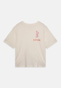 T-shirt couleur crème fabriqué en matériau doux ; présente des manches courtes et un col rond. Texte brodé "JUST LOVE" avec un design de fleur rose.