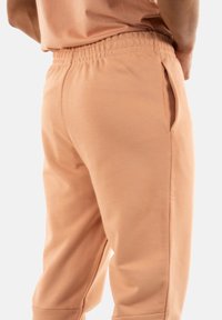 Pantalones jogger de color durazno con cintura elástica y bolsillos laterales, confeccionados en una tela suave con una textura lisa y un corte ajustado.