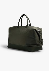 Bolsa de lona de color verde oliva, hecha de material duradero, con asas cortas, una correa de hombro desmontable y una textura suave con costuras de acento.