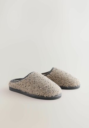 Beige fleece slippers with a soft texture, rounded toe, and black rubber soles. Accented with a gray trim along the opening.