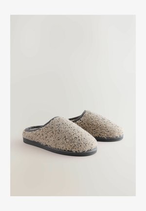 Beige fleece slippers with a soft texture, rounded toe, and black rubber soles. Accented with a gray trim along the opening.