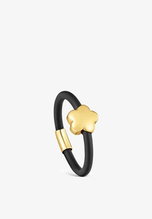 Bague à bande noire avec un pendentif en forme de fleur dorée et un accent doré assorti sur un fond blanc.
