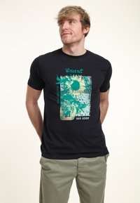 Svart bomullströja med grafisk design av solrosor och texten "Vincent Amsterdam Van Gogh" i turkosa och krämfärgade nyanser.