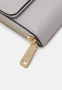 Gray leather pouch with a gold zipper and branded pull tab, showing smooth texture and contrasting stitching along the edges.
