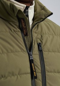 Olive green puffer jacket with a high collar, featuring black zippers and a logo tag reading "PME LEGEND." Textured quilted design.