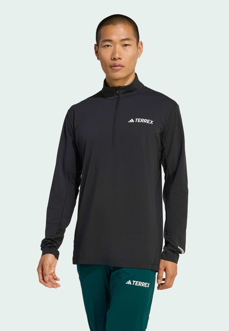 Black long-sleeve quarter-zip top in lightweight material, features a TERREX logo on the chest, with fitted design and textured sleeves.