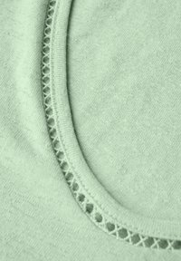 Jasnozielona dzianina o gładkiej teksturze z ozdobnym, perforowanym wykończeniem wzdłuż dekoltu.