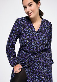 Abito floreale con base nera e motivi di fiori viola e blu, maniche lunghe, scollatura a V e design drappeggiato.