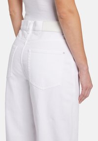 Pantaloni bianchi in denim a vita alta con una vestibilità rilassata, dotati di due tasche posteriori e un'etichetta rettangolare in pelle sulla vita.