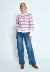Multicolore trui met golvende patronen in roze, blauw en wit, met een ronde hals en pofmouwen; gecombineerd met hoge taille blauwe jeans.