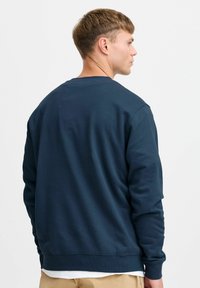 Hanorac bleumarin cu mâneci lungi și guler rotund. Fabricat dintr-un material moale, cu o textură simplă, netedă, fără modele.