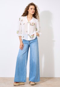 White button-up shirt with floral embroidery, paired with light blue wide-leg jeans and platform espadrilles. Soft, textured fabric.