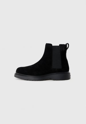 Black suede Chelsea boots with elastic side panels and a pull tab. Thick black rubber sole for traction, minimalist design.