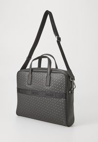 Sac à ordinateur portable noir en synthétique avec un motif texturé, deux poignées supérieures, une bandoulière ajustable et une bande de logo contrastante.