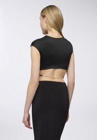 Crop top nero con maniche corte, presenta una schiena con taglio e un accento in catena metallica. Texture liscia, design aderente.