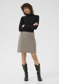 Sort langærmet turtleneck kombineret med en knælang brun hundtandstribet nederdel og sorte læder ankelstøvler med spidse tæer.