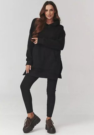 Czarny oversize hoodie wykonany z miękkiego materiału, w zestawie z czarnymi legginsami i masywnymi czarnymi butami na platformie. Posiada kaptur i boczne rozcięcia.