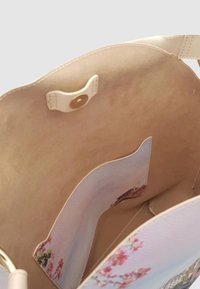 Interno di una borsa a tracolla in pelle chiara con una texture liscia, caratterizzato da una chiusura a scatto e una tasca laterale con un motivo floreale.