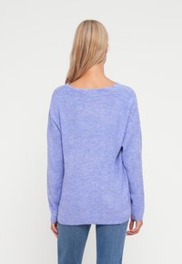 Lys lilla strikket genser med lange ermer og vid hals, med en løs passform og ribbet tekstur, sammen med blå jeans.