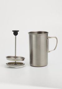Tasse en acier inoxydable avec une poignée, accompagnée d'un presse-français en métal avec un piston et une base. Texture lisse, forme cylindrique, finition mate.