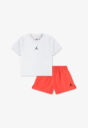 Valge T-särk musta Jordani logoga ja punased lühikesed püksid musta logoga; puuvillane materjal, lühikesed varrukad, elastne vöökoht, sportlik disain.