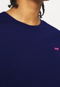 Námořnická modrá bavlněná tričko s kulatým výstřihem. Má malé červené logo Levi's na levé straně hrudi. Hladký povrch, krátké rukávy.