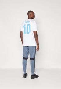 Hvid t-shirt med "Messi" og nummeret "10" i lyseblå. Akkompagneret af grå sportbukser med sorte detaljer og striber.