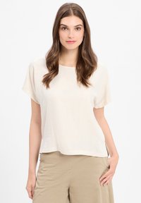 Lichtbeige top met korte mouwen, een ronde halslijn en een losse pasvorm. Glad textuur, ontspannen silhouet, zijsplitten en een minimaal ontwerp.