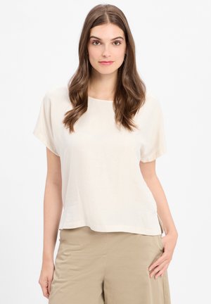 Lichtbeige top met korte mouwen, een ronde halslijn en een losse pasvorm. Glad textuur, ontspannen silhouet, zijsplitten en een minimaal ontwerp.