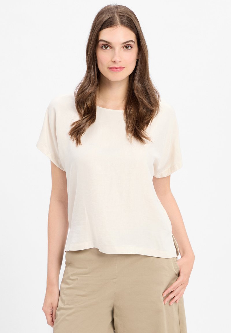 Lichtbeige top met korte mouwen, een ronde halslijn en een losse pasvorm. Glad textuur, ontspannen silhouet, zijsplitten en een minimaal ontwerp.